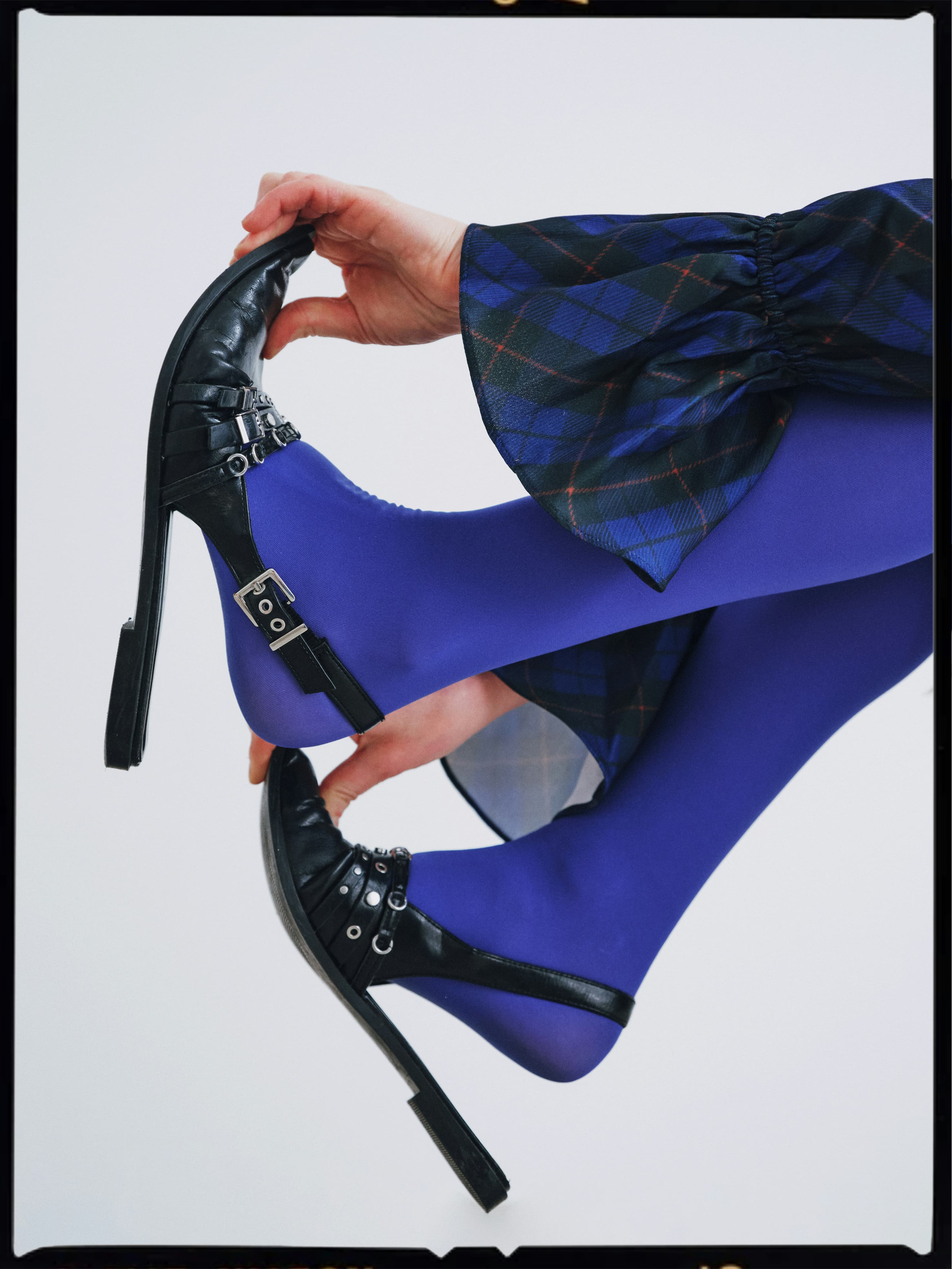 Hand adjusting a strappy heel over bright blue tights